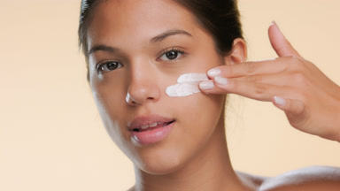 Female model applies cream on face using two fingers