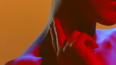 Woman in blue red gel light touches neck and face skin