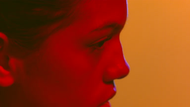 Woman in red light touches neck looks aside back view