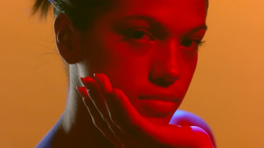 Young beauty in red-blue light rests chin on palm