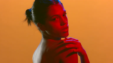 Woman in red gel light looks over shoulder touches skin