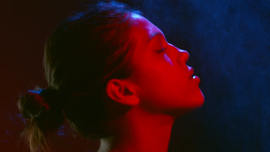 Female model in red led light sprays perfume inhales