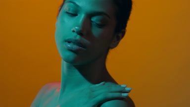 Woman in teal light touches shoulder looks over it