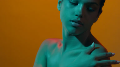 Skincare model in teal led gently touches shoulder looks