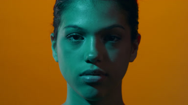 Woman in teal light opens eyes and looks at camera