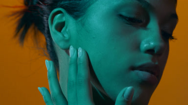 Beauty model in cyan gel light slides fingers up cheek