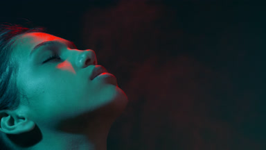 Young model in red & teal light sprays fragrance with pleasure