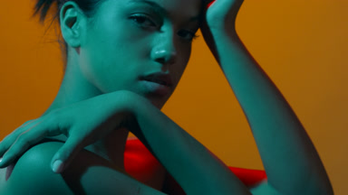 Beauty model in teal & red gel light touches face profile