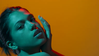Young beauty in cyan & red poses hand on shoulder & face