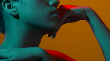 Young model in red & cyan light touches face profile view