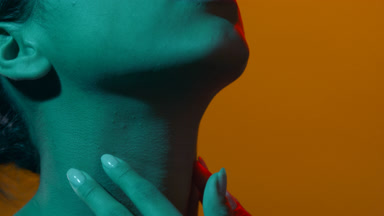Young woman in cyan & red led lighting touches her throat