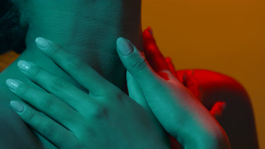 Young female in red & orange led sensually touches throat