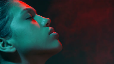 Model in red & teal light sprays fragrance profile sitting