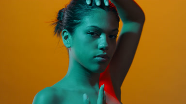 Young woman in red & cyan led touches head and face posing