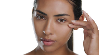Young Latina caresses under eye, illustrating elastic, firm skin