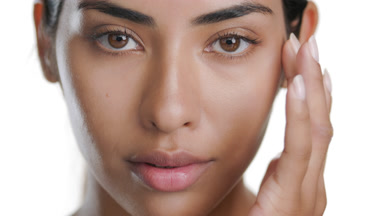 Mid-brown skinned Latin woman strokes cheek, clean skin