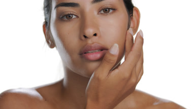 Young Latin woman strokes cheek downward, reveals matte skin