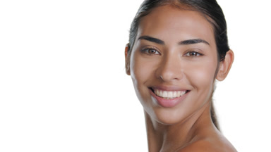 Medium-brown-skinned woman smiles over shoulder, clear skin