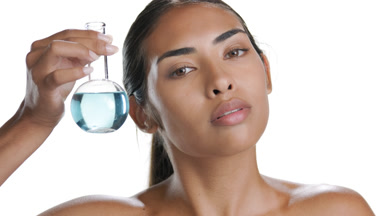 Young Hispanic lady holds round flask with blue liquid near face
