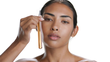 Brunette Hispanic woman holds tube with orange liquid by face
