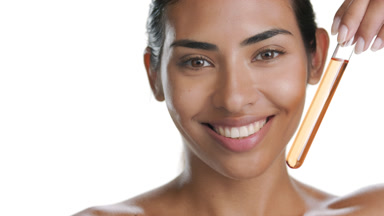 Tan skinned woman smiles, holds test tube with orange liquid