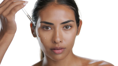 Youthful Latin brunette applies face serum on cheek