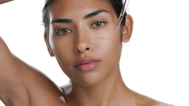 Young Latina applies serum under eye, hand over head