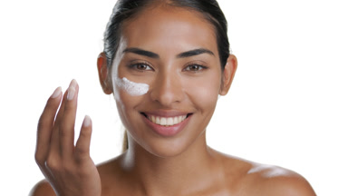 Dark-eyed Latin brunette applies cream on cheek, smiles