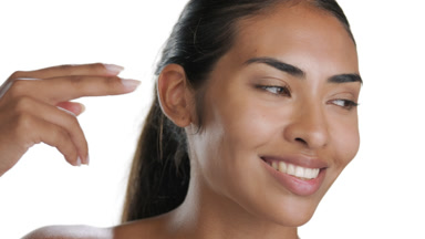 Youthful Latin model strokes under-eye, smiles, pure skin