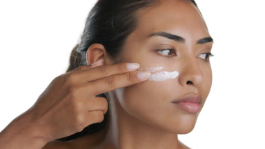 Stylish young Hispanic woman applies face cream, looks aside