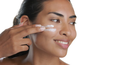 Vibrant young Latin woman applies facial cream, looks aside