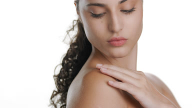 Latina with fair skin strokes shoulder, gazes at camera