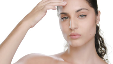 Green-eyed fair Latina strokes face, showing clear radiant skin