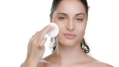 Green-eyed brunette wipes cheek with cotton pad, clean skin