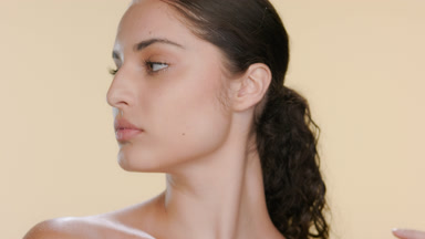 Light-complexioned Latina strokes clavicles, looks aside