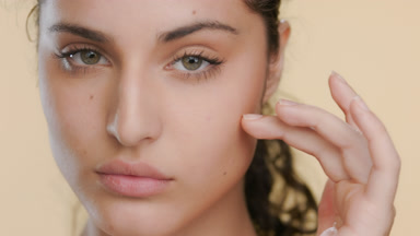 Green-eyed fair Latina strokes cheek under eye, balanced skin
