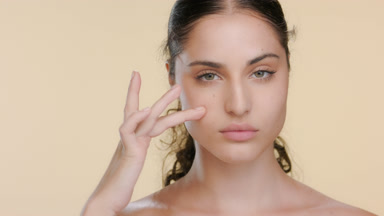 Young Hispanic woman strokes under eye, bright skin attention