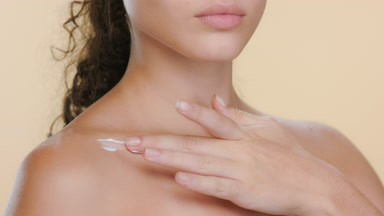 Spanish woman with curls applies cream on clavicle