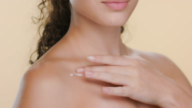 Hispanic brunette applies cream on clavicle, smiling
