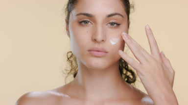 Hispanic woman with fair skin applies cream on cheek