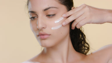 Light-skinned brunette Latina applies face cream, looks aside