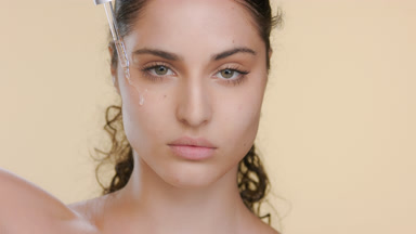 Fair-skinned Latin woman applies serum under eye, hand raised