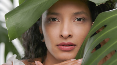 Woman turning face to camera moving plant leaf aside with hand