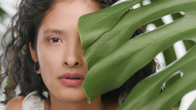 Beauty model surrounded by plants opens eyes and looks at camera