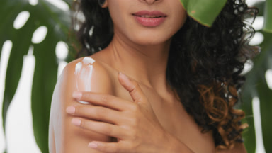 Beautiful latin woman applies organic body cream on her shoulder