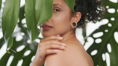 Latin american beauty model touching her shoulder among leaves