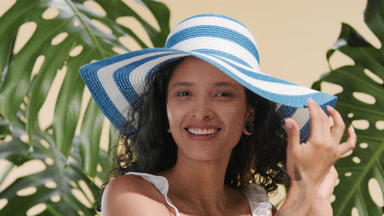 Positive skincare model putting on sun hat