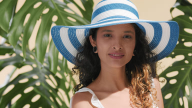 Latin woman in white-blue sun hat among plants turns to camera