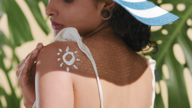 Skincare woman in sun hat applies sun cream on her shoulder