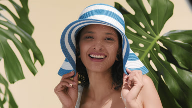 Latina model playfully pulling brims of her sun hat among leaves